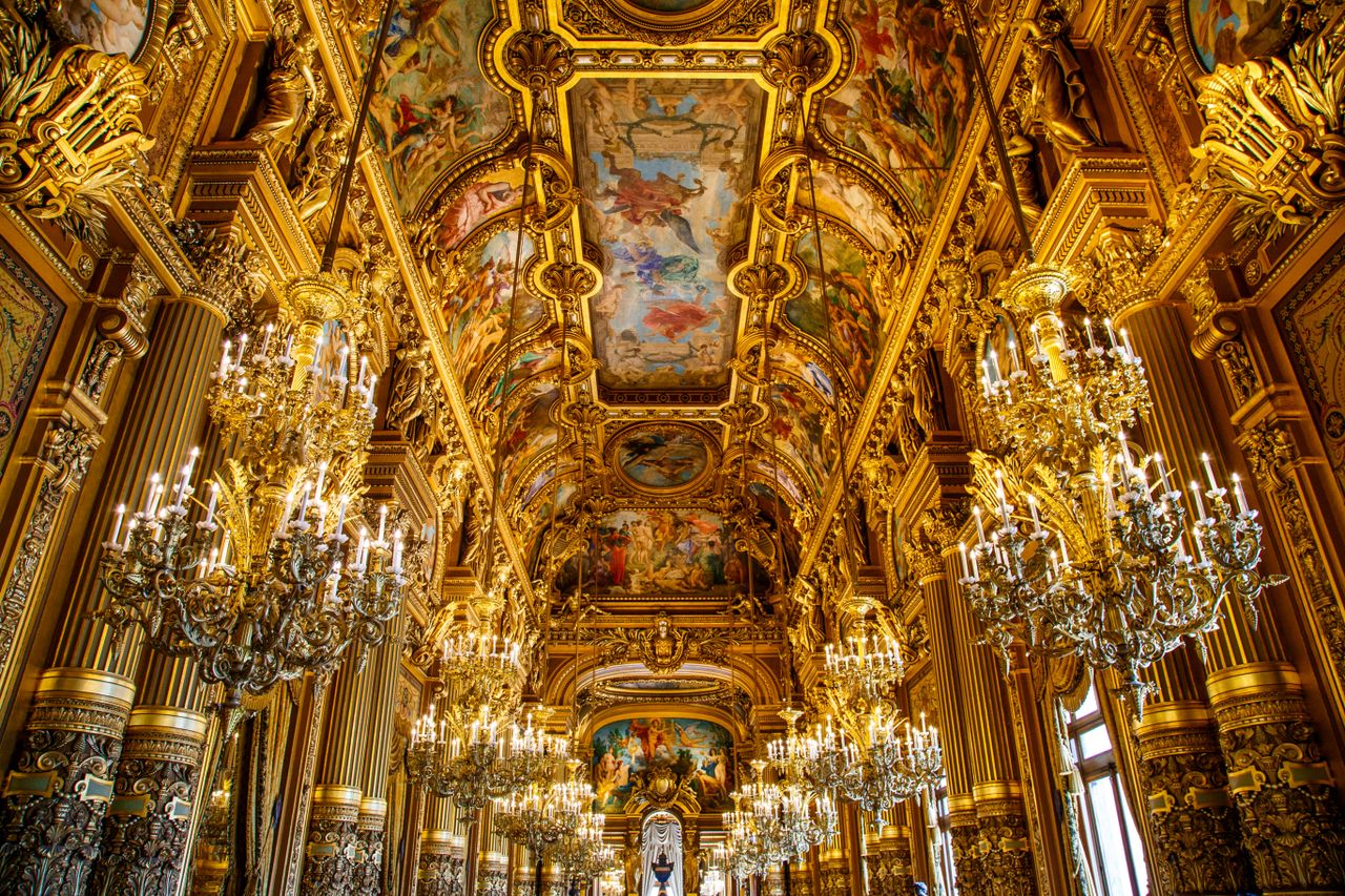 Opulent golden hallway with grand chandeliers and intricate ceiling artwork in a classic Parisian palace.